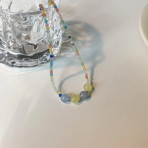 Rainbow beaded choker necklace with cat eye stones displayed on a textured glass cup