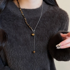 Detail of tiger eye beaded Y-necklace worn on model with irregular brown stone accents