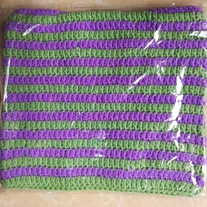 Macro detail of purple and green striped knit beanie inside transparent packaging