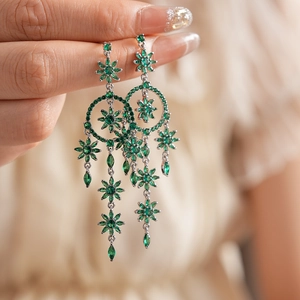 Silver flower tassel earrings with green emerald-cut stones held by a model