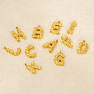 Gold alphabet initial pendants with hammered bubble texture on a beige background