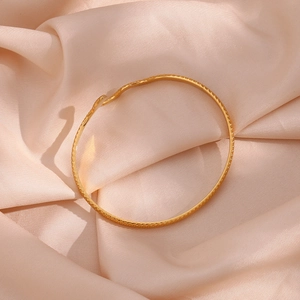 Close-up of gold stainless steel bangle with diamond pattern texture on silk