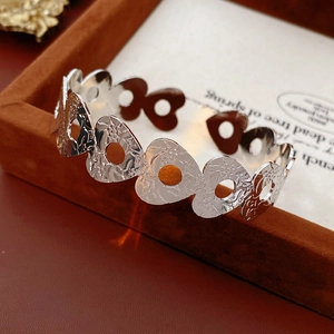 Detail of silver heart floral hollow embossed bangle on a brown velvet display