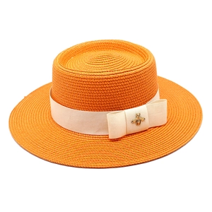 Detail of orange woven straw boater hat with cream ribbon bow and golden bee ornament