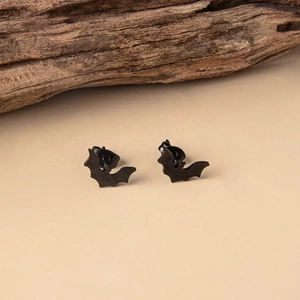 Close-up of minimalist black bat-shaped stud earrings on a natural wood surface