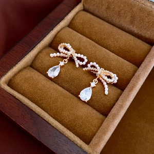 Macro shot of bowknot earrings with pearls and pear-cut zircon in a red velvet box