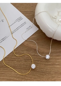 Close-up of gold and silver zircon pendant necklaces with fine snake chains on a desk