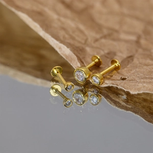 Three gold S925 silver stud earrings with clear round diamonds on a mirror surface