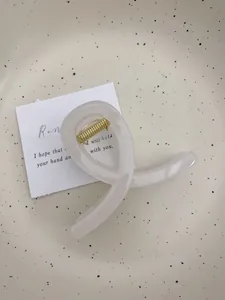 Gros plan d'une pince à cheveux minimaliste en acétate crème sur un plateau en céramique
