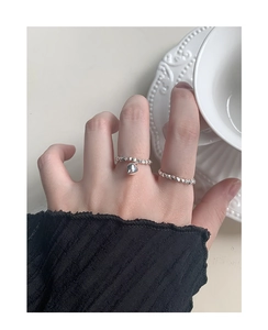 Close-up of textured silver rings on hand featuring a delicate heart pendant detail