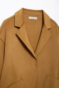 Close-up detail of caramel wool coat showing lapel collar texture and interior brand label
