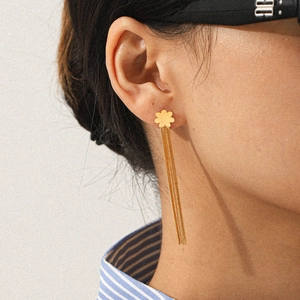 Close-up of golden flower stud earrings with long chain tassels worn by a female model