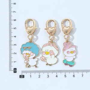 Three cute cartoon duck enamel keychains with golden heart lobster clasps on white background