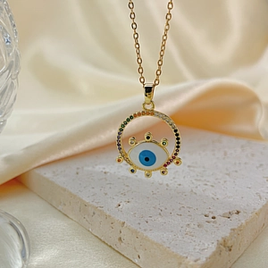 Macro shot of evil eye pendant with multicolor zircons on gold chain over silk fabric