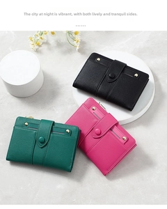 Three leather bifold wallets in black, pink, and green displayed on a marble platform