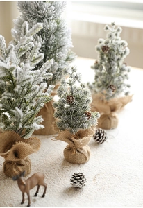 Close-up of mini snowy Christmas trees with pine cones and rustic burlap bases