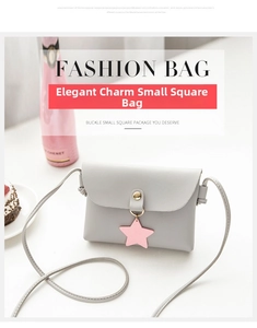 Detail of light gray crossbody bag with gold buckle and pink star charm on a table
