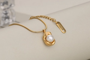 Macro shot of irregular gold peanut pendant with round white pearl on snake chain