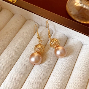 Macro shot of elegant fishtail pearl earrings with hollow gold sphere in a beige velvet box