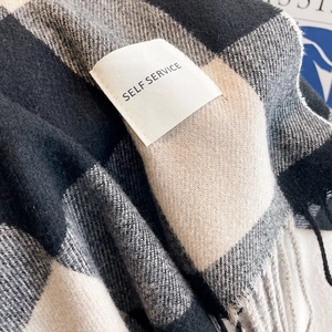 Detailed close-up of plaid cashmere scarf texture with tassel edges and woven logo label