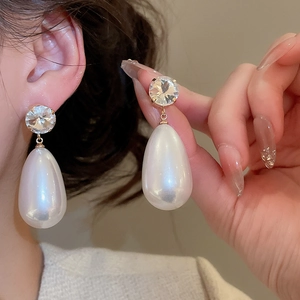 Detailed view of large teardrop pearl earrings with brilliant round zircon on model