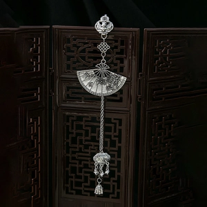 Detail of vintage silver plum blossom fan pendant with tassels on a wooden screen
