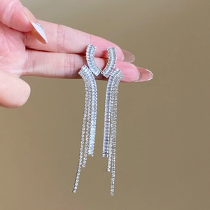 Détail de boucles d'oreilles pendantes argentées avec strass brillants tenues à la main