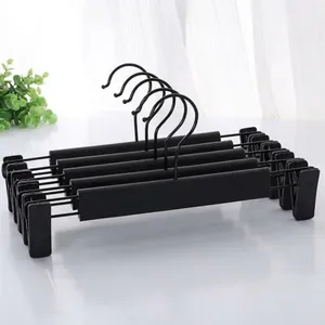 Macro detail of five matte black adjustable metal pants hangers with sliding clips