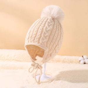 Detailed cable knit pattern on a beige baby winter hat with soft faux fur pom and ties