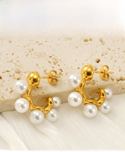 Detail view of C-shaped gold pearl earrings on elegant beige stone and silk background