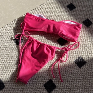 Flat lay of a rose pink bandeau bikini with side-tie bottoms on a textured rug