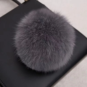 Détail d'un pompon en fourrure de renard grise fixé sur un sac en cuir noir de luxe
