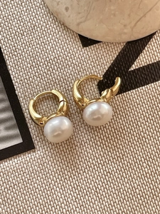 Detail shot of elegant gold pearl hoop earrings on a minimalist beige fabric background