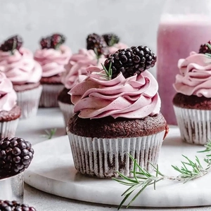 Close-up of a chocolate cupcake with purple frosting and fresh blackberries in a printed liner