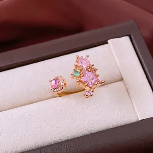 Elegant gold open ring with pink star zircons and green gemstone on beige velvet