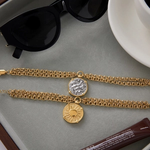 Detail view of double-layered gold titanium steel coin bracelets on a grey tray