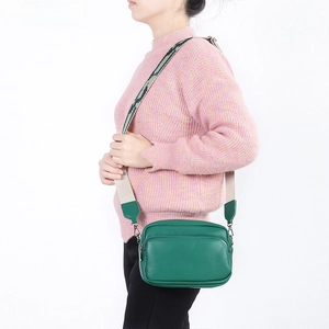 Dettaglio della borsa a tracolla in pelle verde con ampia tracolla jacquard indossata da modella