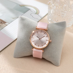 Détail d'une montre or rose avec bracelet en silicone rose et index en strass sur coussin