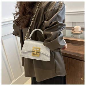 Detail of light gray suede handbag with gold metal lock and chain strap on model
