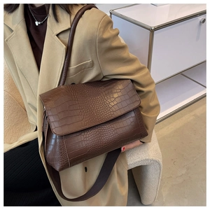 Detail of brown crocodile pattern shoulder bag with flap design and wide strap on model