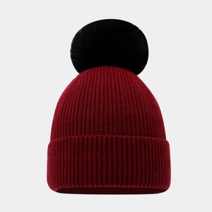 Detail of dark red ribbed knit beanie featuring a fluffy black faux fur pompom top