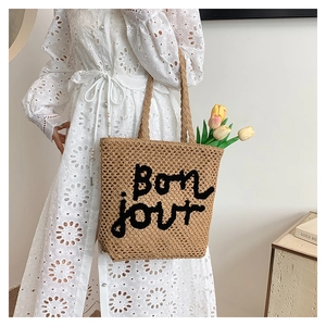 Detail of hand-woven straw tote with black Bon jour embroidery and natural texture