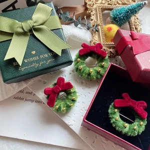 Three Christmas wreath brooches with red bows and green plush texture in a gift box