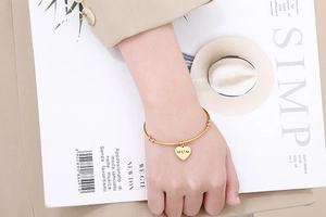 Gros plan d'un bracelet doré avec pendentif cœur gravé MOM porté par une femme