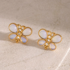 Macro shot of gold butterfly stud earrings with white gemstones on a grey stone surface