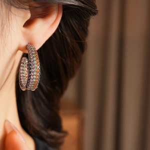 Close-up of rainbow zircon C-shaped earrings worn by a model in a warm setting