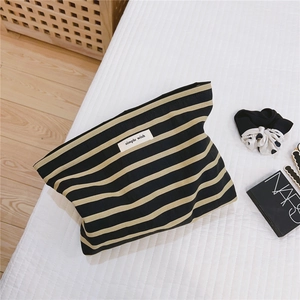 Detail shot of striped cotton canvas makeup bag with Simple Wish label on white bedding