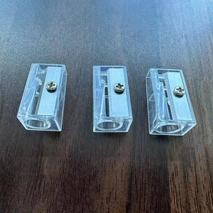 Close-up of three transparent plastic pencil sharpeners with metal blades on a wood surface