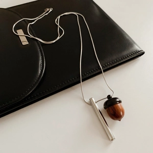 Detail of wooden acorn pendant on silver chain necklace over black leather surface