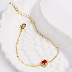Détail d'un bracelet cœur doré avec pierres de zircon rouges et cristaux micro-pavés